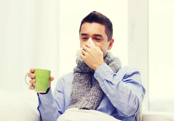 Zieke man met griep drinken thee en blazen neus — Stockfoto