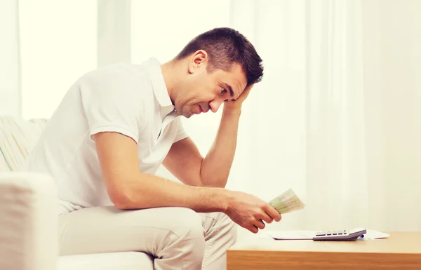 Hombre con dinero y calculadora en casa — Foto de Stock