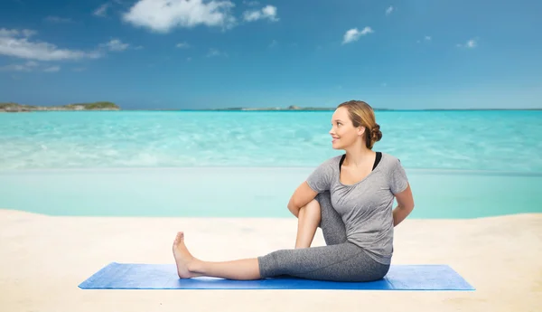 Женщина делает yoga в твист позе на циновке над пляжем — стоковое фото