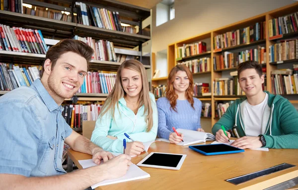 Gelukkig studenten schrijven naar laptops in bibliotheek — Stockfoto