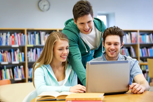 Estudiantes felices con portátil en la biblioteca —  Fotos de Stock