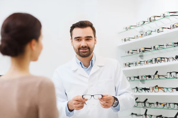 Женщина и оптик показывает очки в магазине оптики — стоковое фото