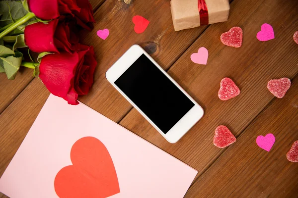 Close-up de smartphone, presente, rosas vermelhas e corações — Fotografia de Stock