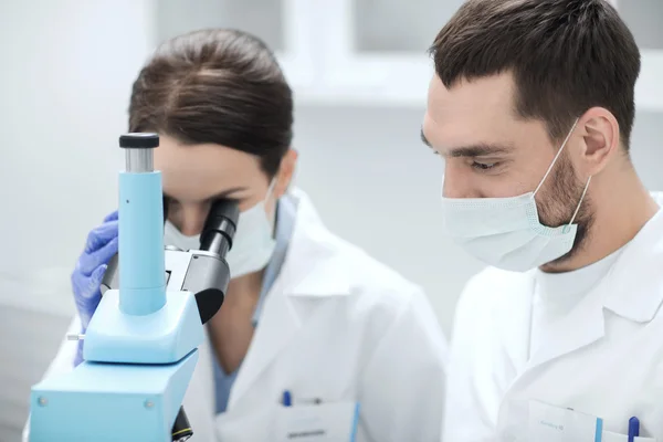 Científicos con máscaras mirando al microscopio en el laboratorio — Foto de Stock