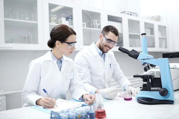 Científicos con portapapeles y microscopio en laboratorio — Foto de Stock