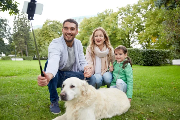 Счастливая семья с собакой, делающей селфи на смартфоне — стоковое фото