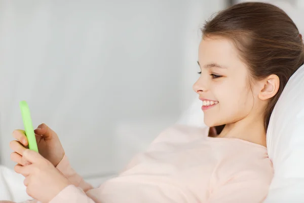 Glad tjej i sängen med smartphone hemma — Stockfoto