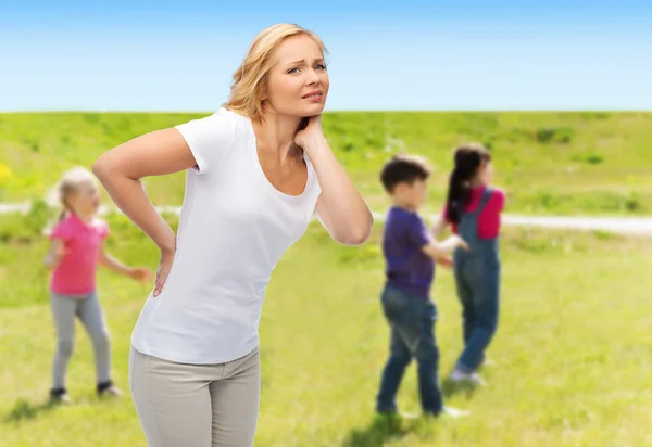 Woman suffering from backache over group of kids — Stockfoto