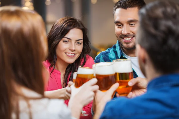 Amigos bebiendo cerveza y tintineo vasos en el pub — Foto de Stock