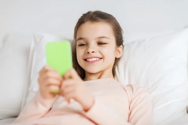 Happy girl lying in bed with smartphone at home — Stock Photo, Image