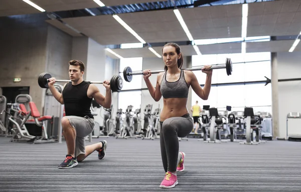 Jonge man en vrouw met barbell in gym training — Stockfoto