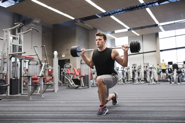 Jovem homem flexionando músculos com barbell no ginásio — Fotografia de Stock