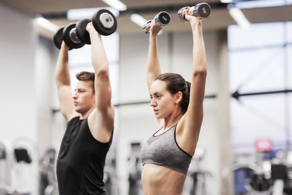 Sonriente hombre y mujer con mancuernas en el gimnasio —  Fotos de Stock