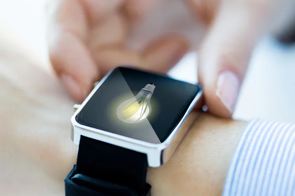 Close up of hands with lightbulb on smartwatch — Stockfoto