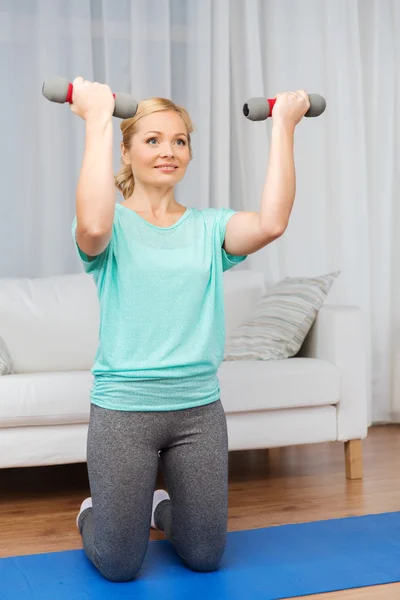 Woman exercising with dumbbells on mat at home — ストック写真