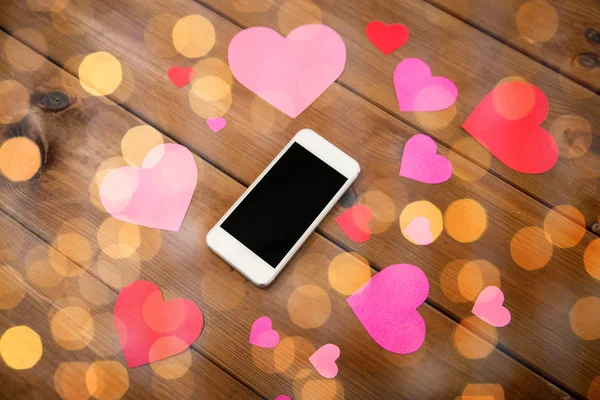 Close up of smartphone and hearts on wood — Stock Photo, Image