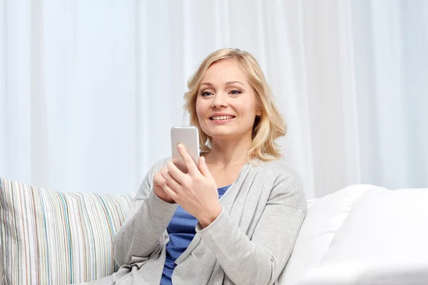 Smiling woman with smartphone texting at home — Stock Photo, Image