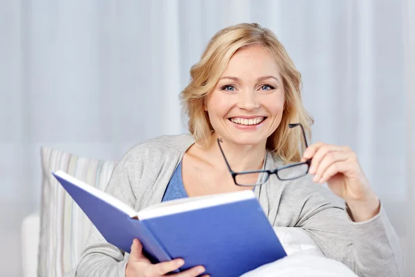 Усміхнена жінка читає книгу і сидить на дивані — стокове фото