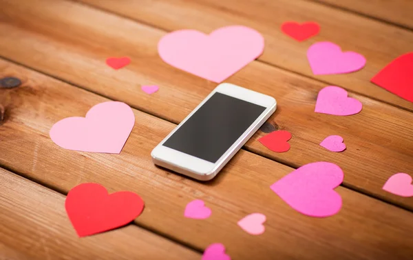 Close up of smartphone and hearts on wood — Stock Photo, Image