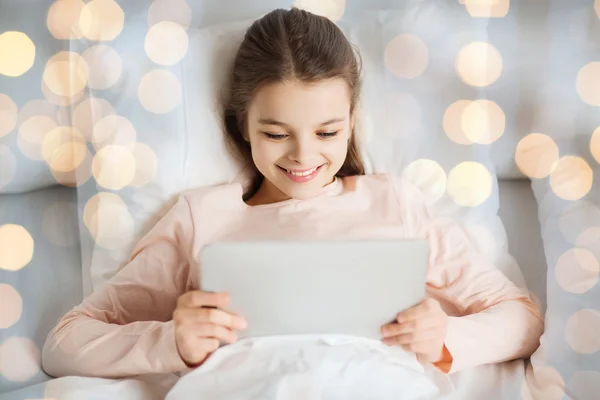 Счастливая девочка, лежащая в постели с планшетным компьютером дома — стоковое фото