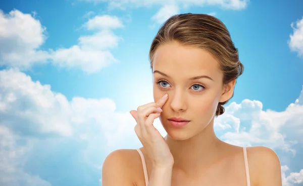 Mujer joven aplicando crema a la cara sobre el cielo azul —  Fotos de Stock