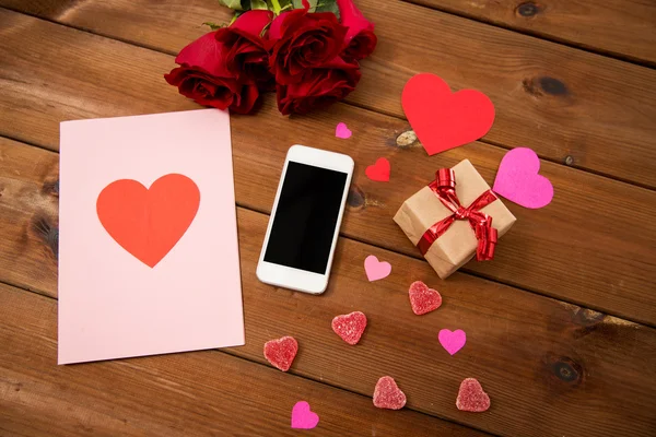 Close-up de smartphone, presente, rosas vermelhas e corações — Fotografia de Stock