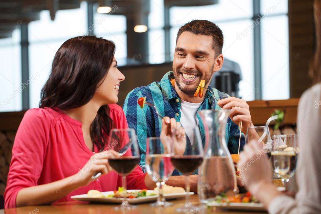Happy couple with friends eating at restaurant Stock Photo by ??Syda