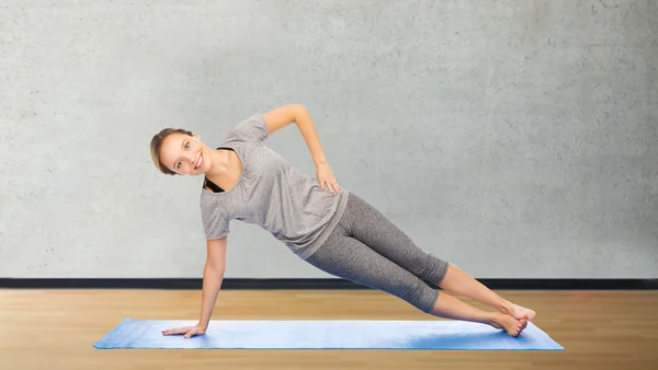 Vrouw maken yoga in zijkant plank pose op de mat — Stockfoto