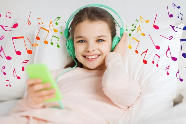 快乐的女孩，在智能手机和耳机的床上 — 图库照片