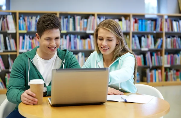 Zadowoleni uczniowie z laptopa w bibliotece — Zdjęcie stockowe