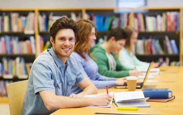 Menino estudante feliz com livros escrevendo na biblioteca — Fotografia de Stock