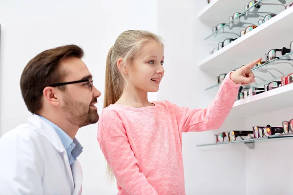 Optician e menina escolhendo óculos na loja de óptica — Fotografia de Stock