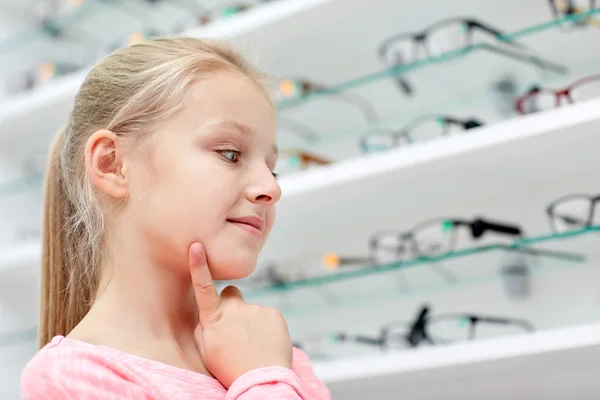Маленькая девочка выбирает очки в магазине оптики — стоковое фото