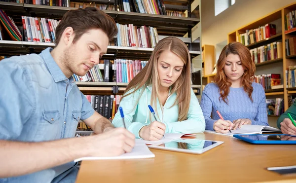 Happy students writing to notebooks in library Royalty Free Stock Photos