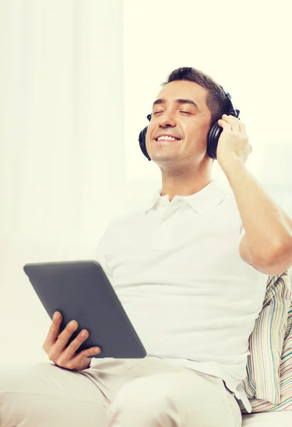 Homme souriant avec tablette PC et écouteurs à la maison — Photo