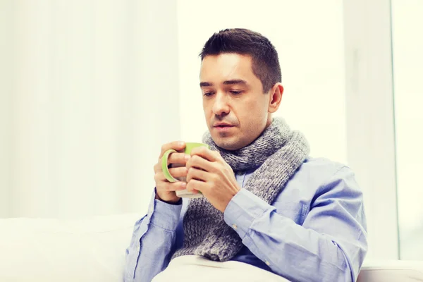 Zieke man met griep drinken van hete thee uit de beker thuis — Stockfoto