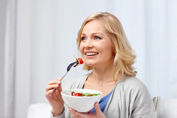 Улыбающаяся женщина средних лет ест салат дома — стоковое фото