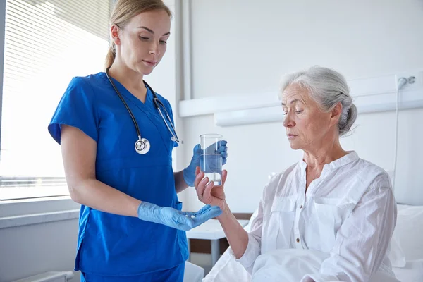 Nurse giving medicine to senior woman at hospital — Stock Photo, Image