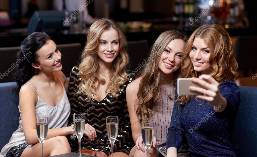 party, technology, nightlife and people concept - smiling friends with  smartphone taking selfie in club. Stock Photo