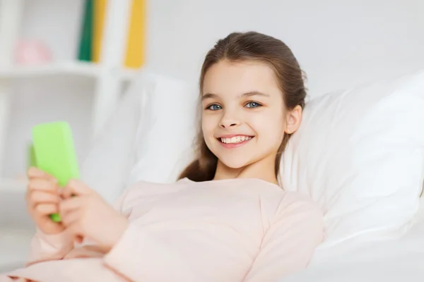 Chica feliz acostada en la cama con teléfono inteligente en casa — Foto de Stock