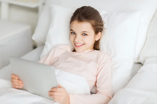 Счастливая девочка, лежащая в постели с планшетным компьютером дома — стоковое фото