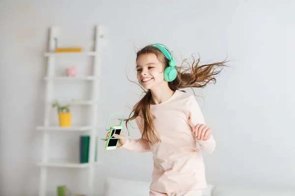 Девушка прыгает на кровать со смартфоном и наушниками — стоковое фото