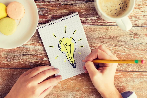 Close up of hands drawing bulb to notebook — Stock Photo, Image