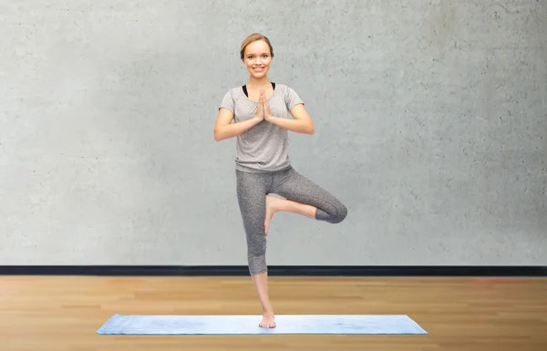 Vrouw maken yoga in boom pose op de mat — Stockfoto