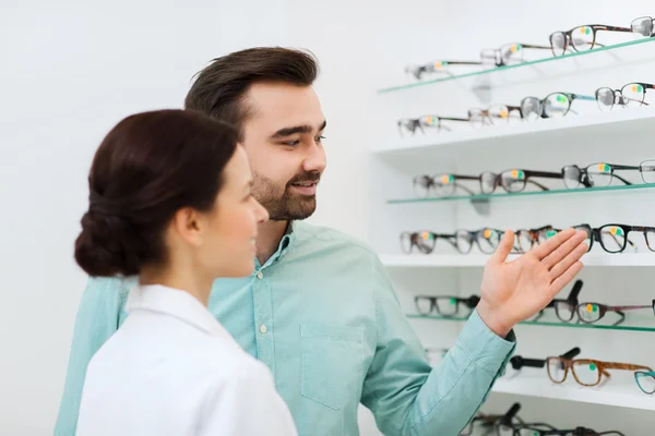 Óptico y hombre la elección de gafas en la tienda de óptica —  Fotos de Stock