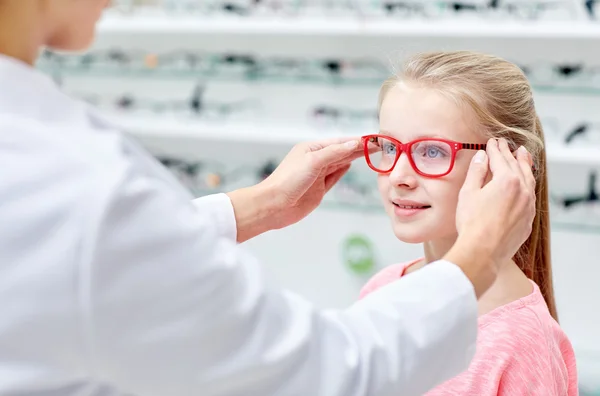 Optician colocando óculos para menina na loja de óptica — Fotografia de Stock