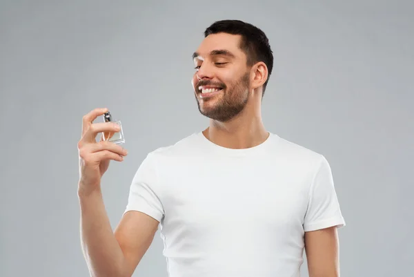 Усміхнений чоловік з чоловічими парфумами на сірому фоні — стокове фото