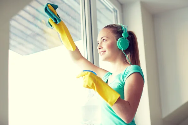 Happy woman with headphones cleaning window — Stock Photo, Image