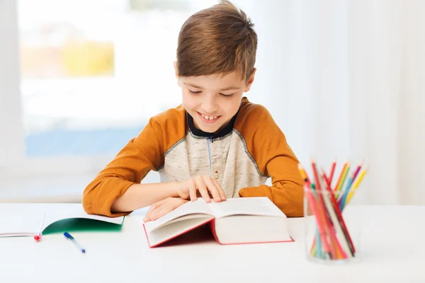 Leende, student pojke läsebok hemma — Stockfoto