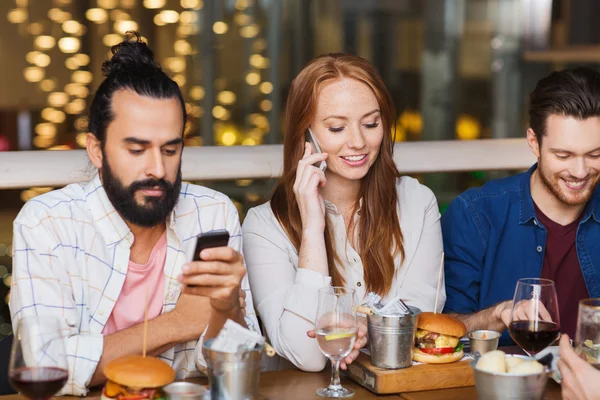Amigos felizes com smartphones no restaurante — Fotografia de Stock